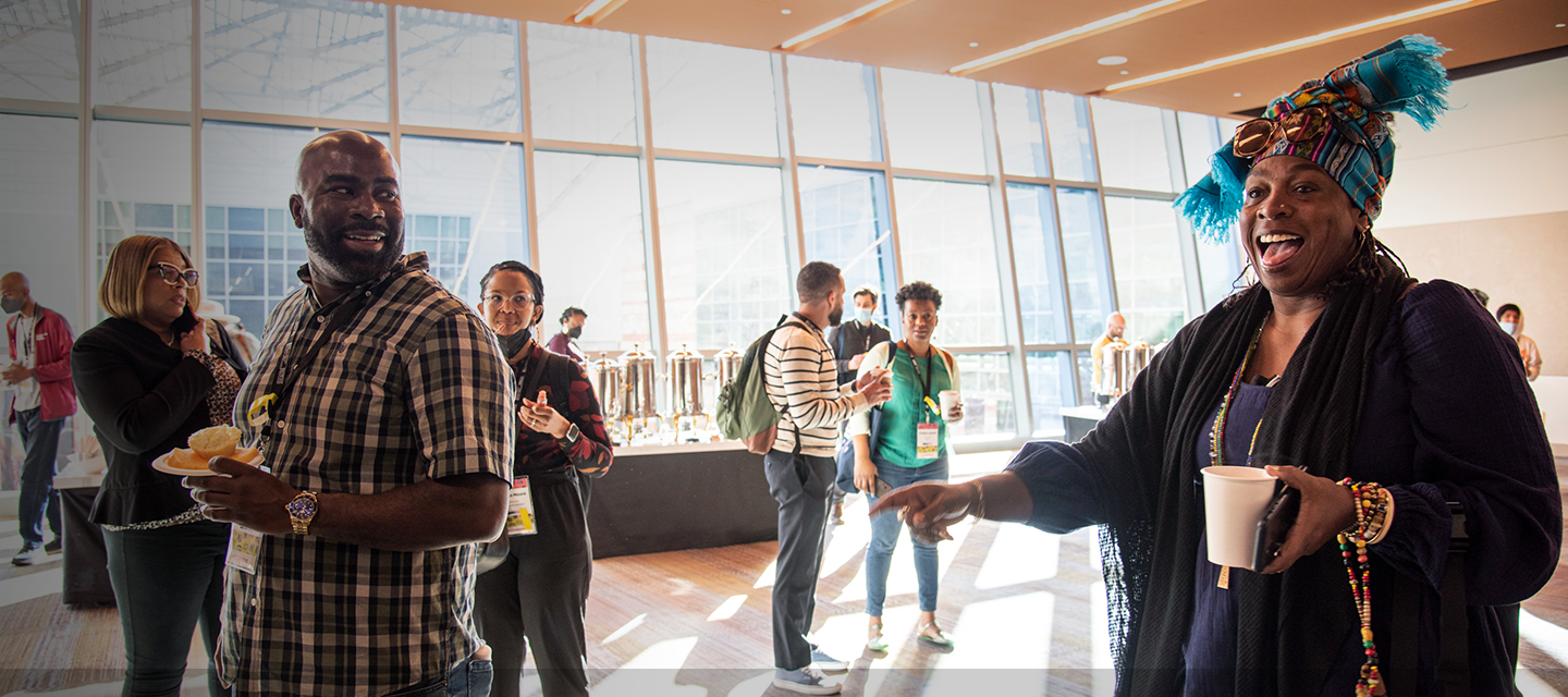 Group of adults outside of a conference room mingling, getting coffee, and smiling