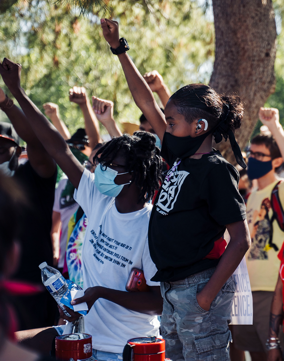 group of young adults with masks on their faces and one fist in the air to show support