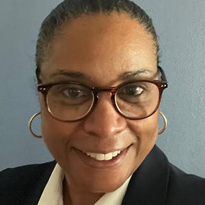 Headshot photo of a Black with hair slicked back wearing glasses, black suit jacket, and opened white-collared shirt