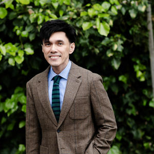 photo of an asian person in a brown jacket and green tie.