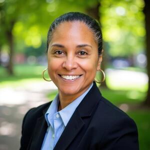 Headshot photo of a Black woman with hair slicked back, black suit jacket, and opened blue-collared shirt