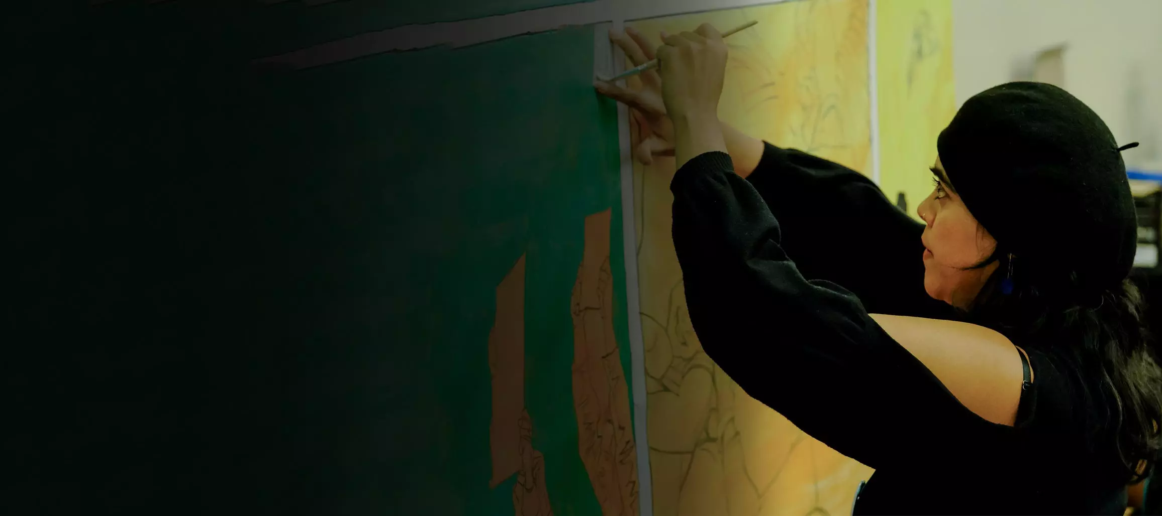 Person in all black carefully painting on paper on a wall.