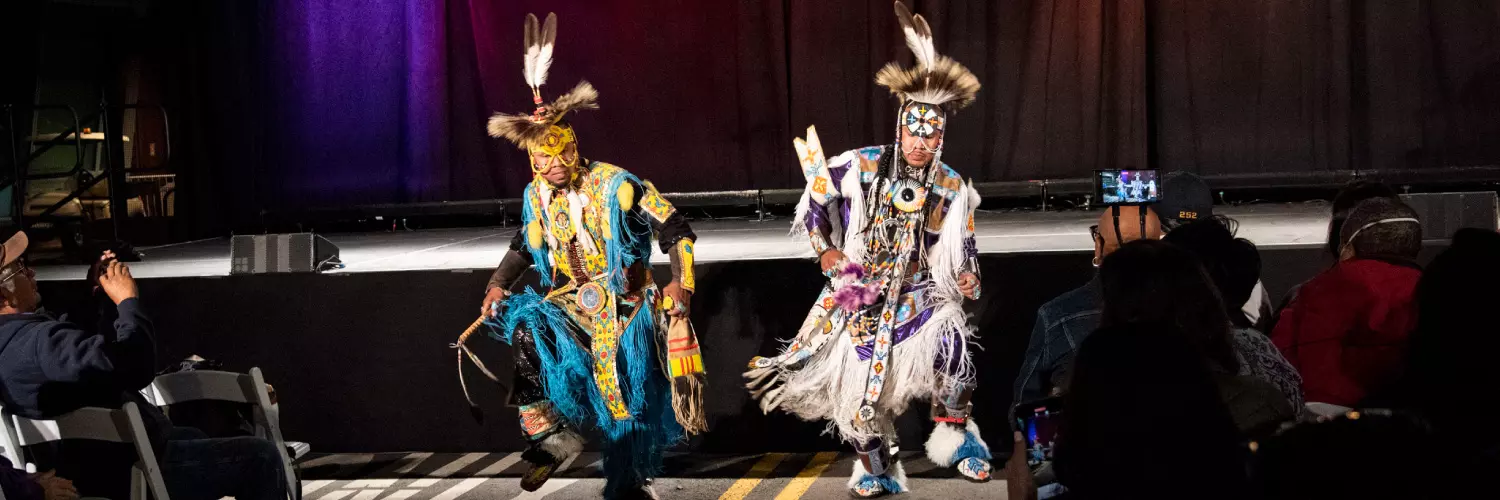 Two Indigenous performers dancing in full dress